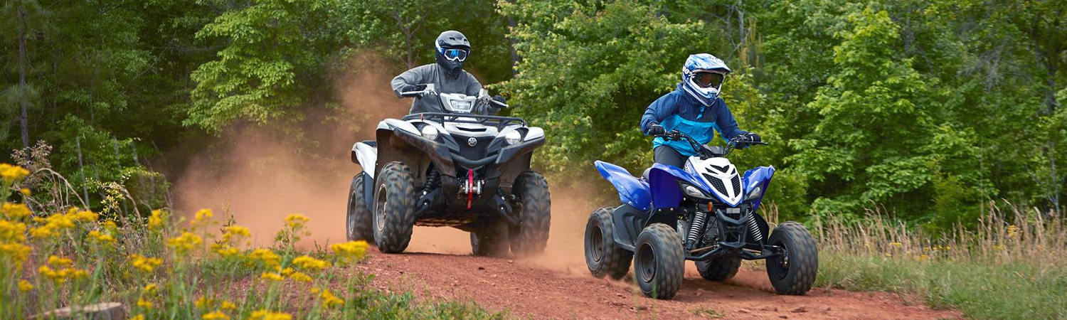 Two people riding Yamaha® Raptor ATVs on a dirt trail in the woods.
